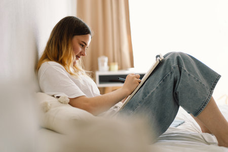 A teenage girl is drawing or doing homework in the bedroom. A teenager studies at home.の写真素材