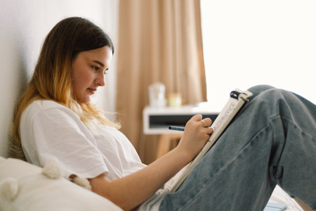 A teenage girl is drawing or doing homework in the bedroom. A teenager studies at home.の写真素材