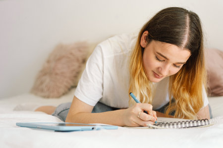A teenage girl is drawing or doing homework in the bedroom. A teenager studies at home.の写真素材