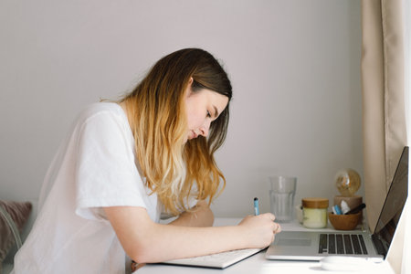 A teenage girl is drawing or doing homework in the bedroom. A teenager studies at home.の写真素材