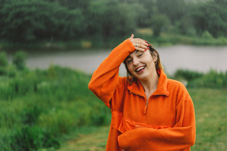 A young girl in an orange sweater is enjoying the rain on a summer day.の写真素材