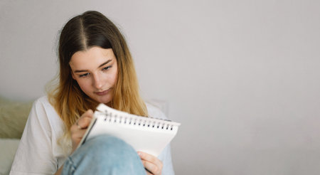 A teenage girl is drawing or doing homework in the bedroom. A teenager studies at home.の写真素材