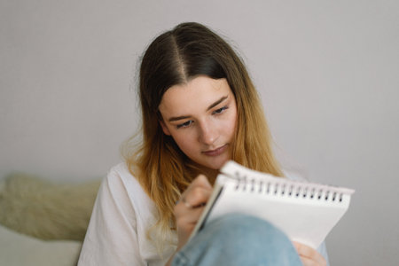 A teenage girl is drawing or doing homework in the bedroom. A teenager studies at home.の写真素材