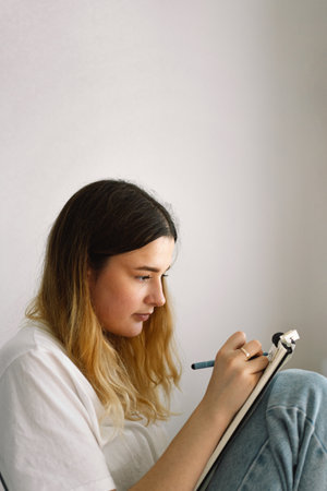 A teenage girl is drawing or doing homework in the bedroom. A teenager studies at home.