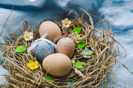 Colorful Easter eggs nestled in a nest surrounded by flowers and straw on a light blue backgroundの写真素材