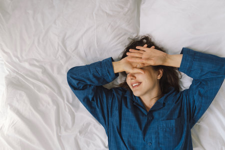 Joyful woman relaxing on soft white bed linen in a cozy bedroom during morning hours