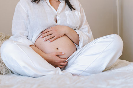 Pregnant woman sitting peacefully on bed in cozy home settingの写真素材