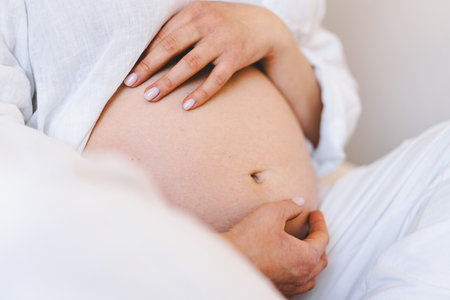 Pregnant woman sitting peacefully on bed in cozy home settingの写真素材
