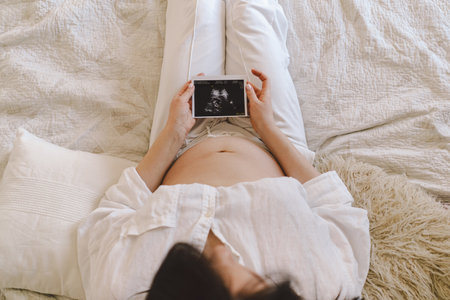 A Woman cradles an ultrasound image against their pregnant bellyの写真素材