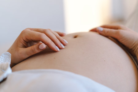 Pregnant woman sitting peacefully on bed in cozy home settingの写真素材
