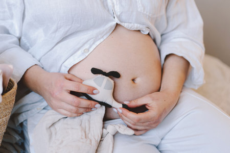 Expectant mother holds basket of baby clothes while gently touching her bellyの写真素材