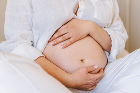 Pregnant woman sitting peacefully on bed in cozy home settingの写真素材