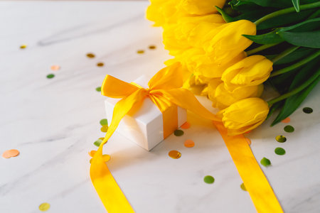 Gift box with long yellow ribbon and tulipsの写真素材