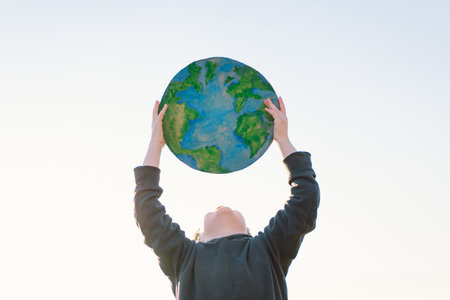 Little boy holding planet in hands against green spring background. Earth dayの写真素材