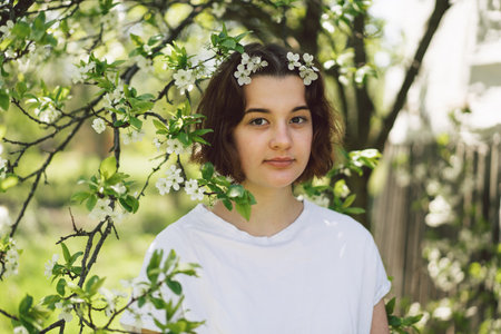 Beautiful teenage girl with spring flowers enjoying nature and laughing on spring gardenの写真素材