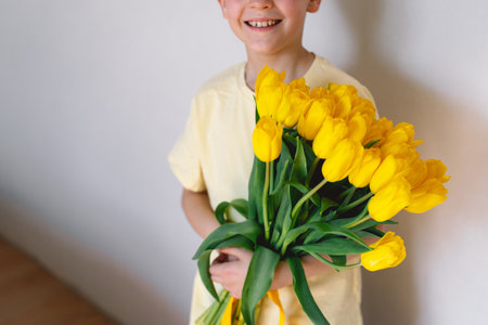 Child joyfully holding a bouquet of vibrant yellow tulipsの写真素材