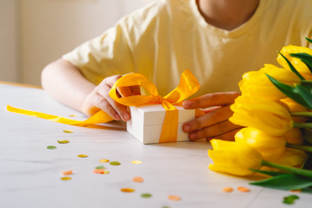 A boy carefully tying a bow on a Mothers Day giftの写真素材