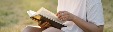 Christian woman holds bible in her hands. Reading the Holy Bible in a field during beautiful sunset.の写真素材