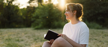 Woman holds book in her hands. Reading the book in a field during sunset.の写真素材