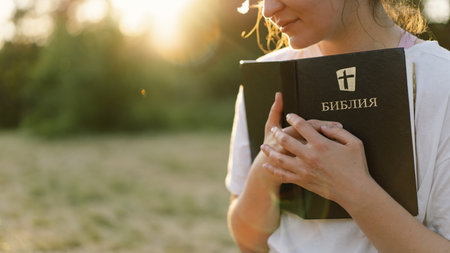Christian woman holds bible in her hands. Reading the Holy Bible in a field during beautiful sunset.の写真素材