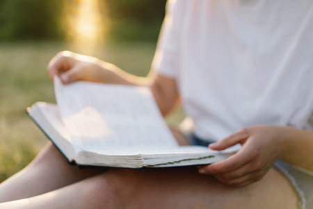 Woman holds book in her hands. Reading the book in a field during sunset.の写真素材