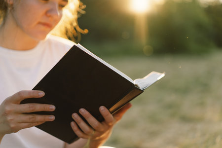 Woman holds book in her hands. Reading the book in a field during sunset.の写真素材