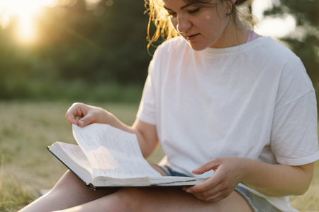 Christian woman holds bible in her hands. Reading the Holy Bible in a field during beautiful sunset.の写真素材