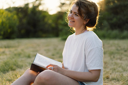Christian woman holds bible in her hands. Reading the Holy Bible in a field during beautiful sunset.の写真素材