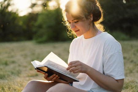 Christian woman holds bible in her hands. Reading the Holy Bible in a field during beautiful sunset.の写真素材