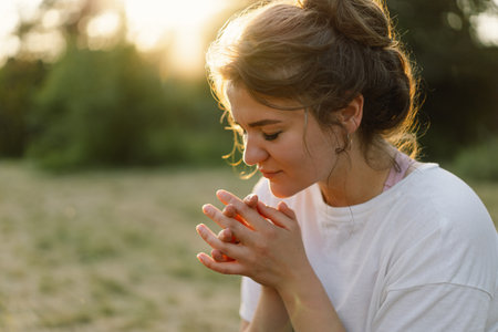 Woman closed her eyes, praying in a field during beautiful sunset. Hands folded in prayer concept for faithの写真素材