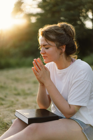 Woman closed her eyes, praying in a field during beautiful sunset. Hands folded in prayer concept for faithの写真素材