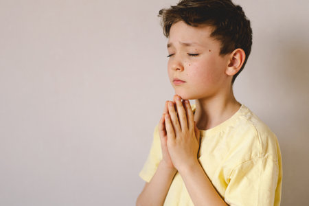 A boy with folded hands in front of him, he prays in his room.