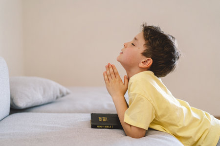 A boy with folded hands in front of him, he prays in his room.