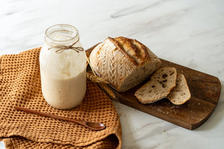 Freshly baked sourdough bread with a jar of starter and rustic clothの写真素材