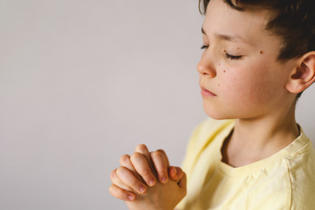 A boy with folded hands in front of him, he prays in his room.