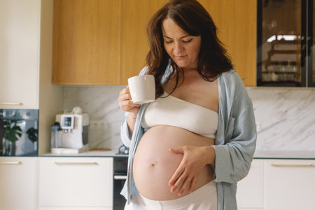 Pregnant woman gently holding her pregnant belly, reflecting on impending motherhoodの写真素材