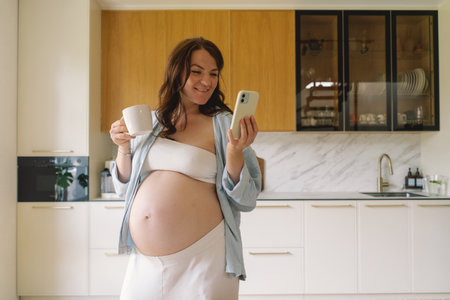 Expecting mother using smartphone in modern kitchen during pregnancy