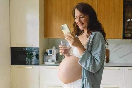 Expecting mother using smartphone in modern kitchen during pregnancy