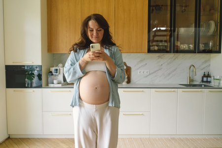 Expecting mother using smartphone in modern kitchen during pregnancy