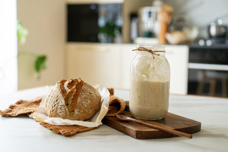 Freshly baked sourdough bread with a jar of starter and rustic clothの写真素材
