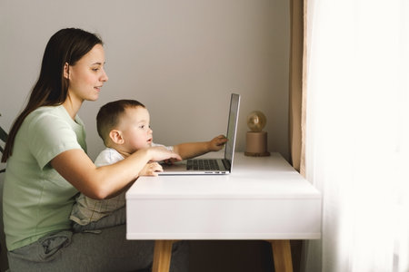 Portrait of happy young mother with little baby using laptop at home.の写真素材