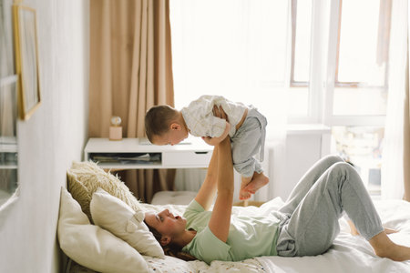 Home portrait of a baby boy with mother on the bed relaxing and playingの写真素材