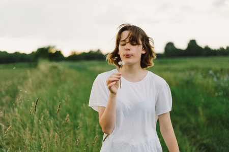 Beautiful teenager girl on the field in green grass and blowing dandelion.