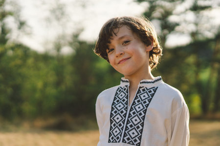 A boy smiles confidently while standing in a sunlit field, wearing a traditional embroidered shirtの写真素材