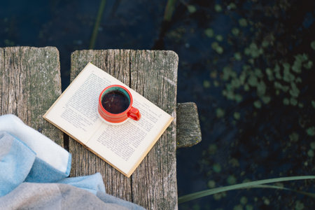 Cup of coffee and book on wooden pier on lake