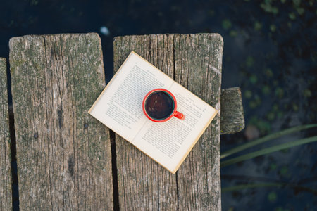 Cup of coffee and book on wooden pier on lake
