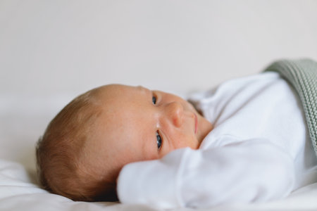 A newborn baby rests on a bed, wrapped in a soft blanket.