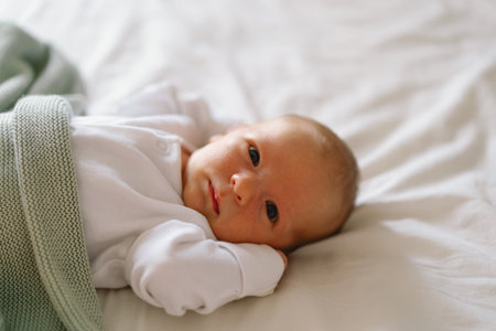 A newborn baby rests on a bed, wrapped in a soft blanket.