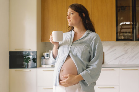 Pregnant woman gently holding her pregnant belly, reflecting on impending motherhoodの写真素材