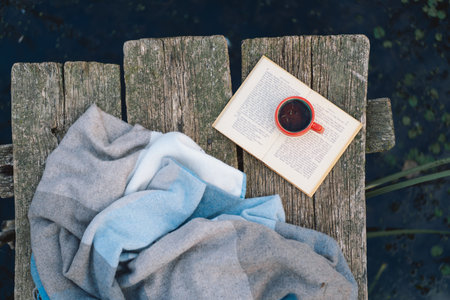 Cup of coffee and book on wooden pier on lake